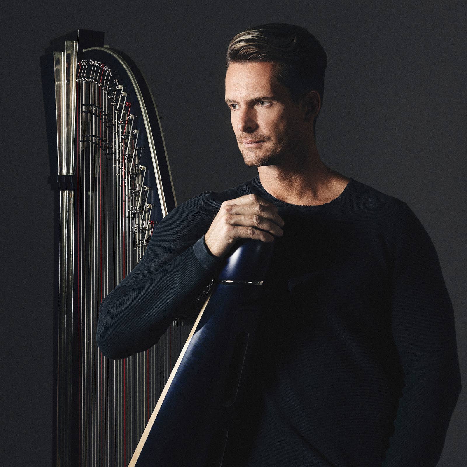 Man holding a harp looking out with dark background lighting.