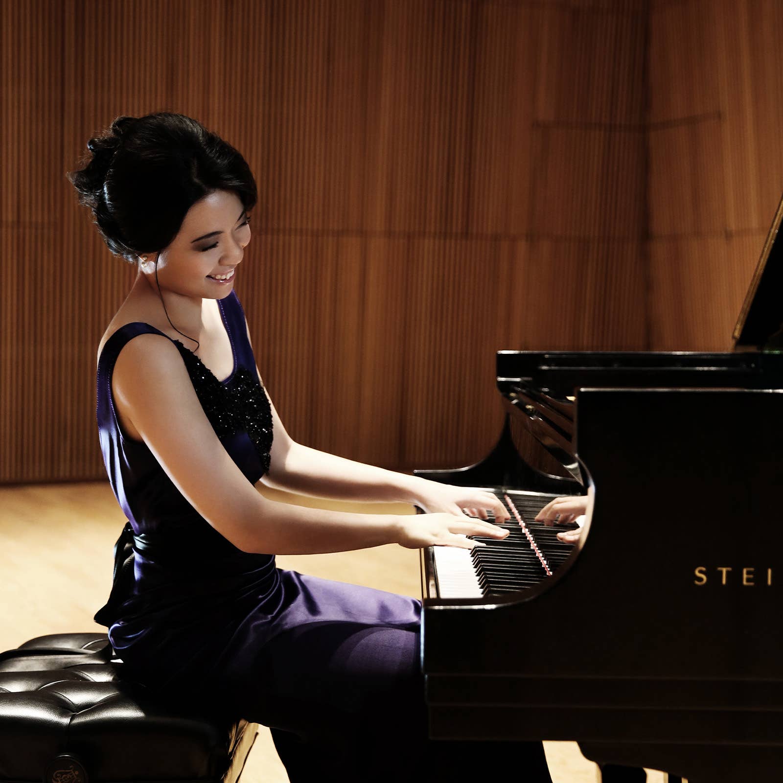 Happy woman smiles while playing a black grand piano in a warmly lit hall