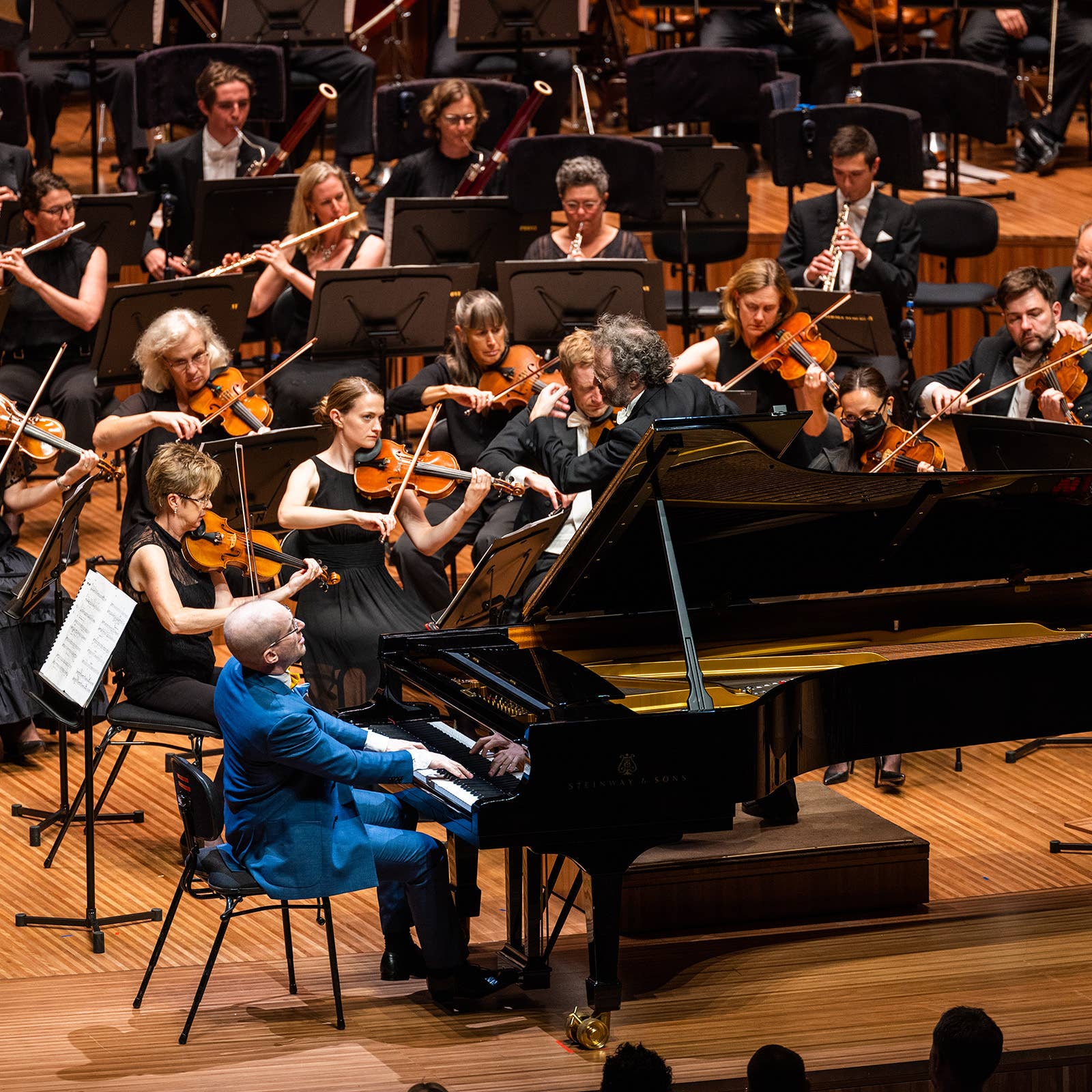 Orchestra performing in a concert hall with violinists and clarinetists surrounding a grand piano player