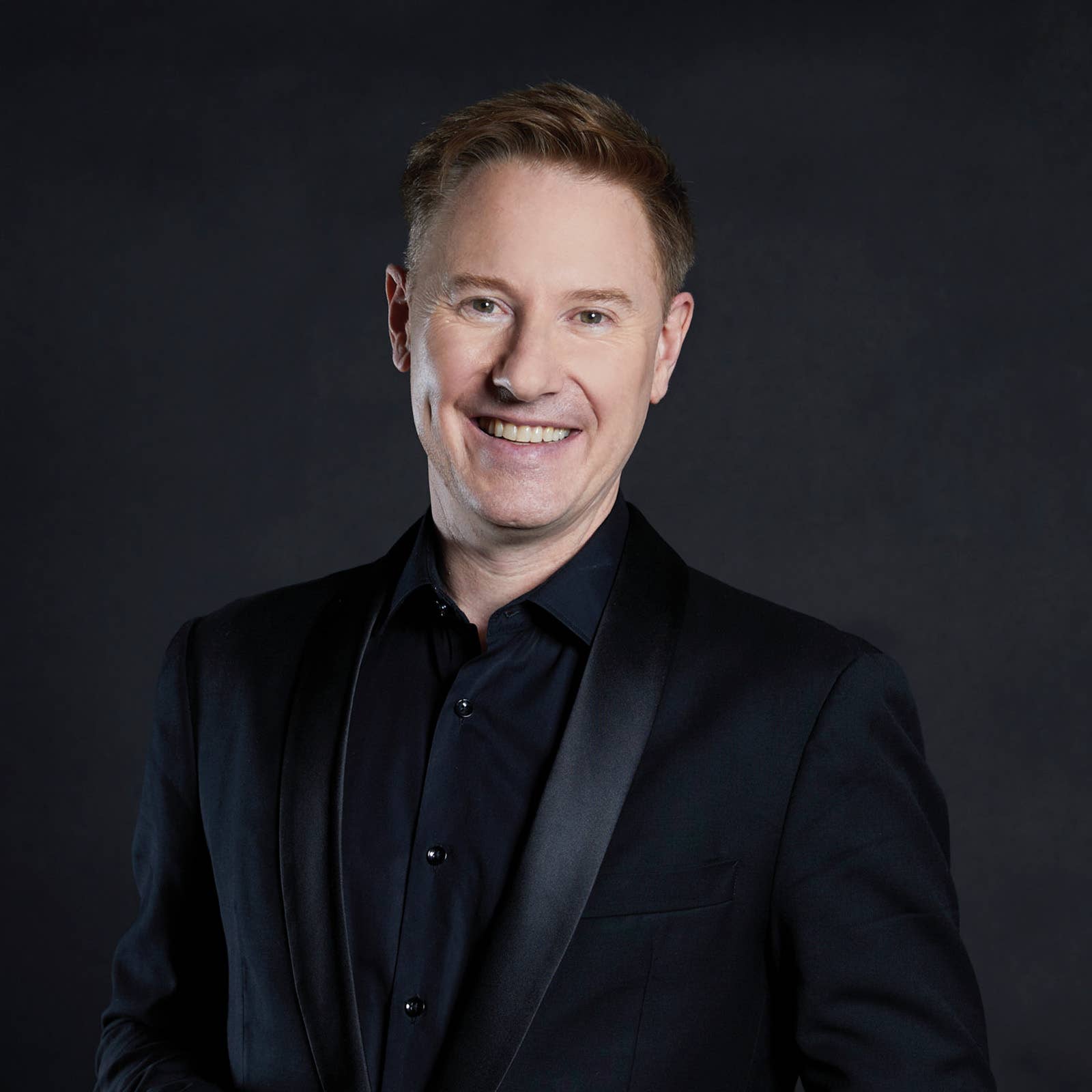 Smiling man in a dark suit and shirt portrait against a dark studio background