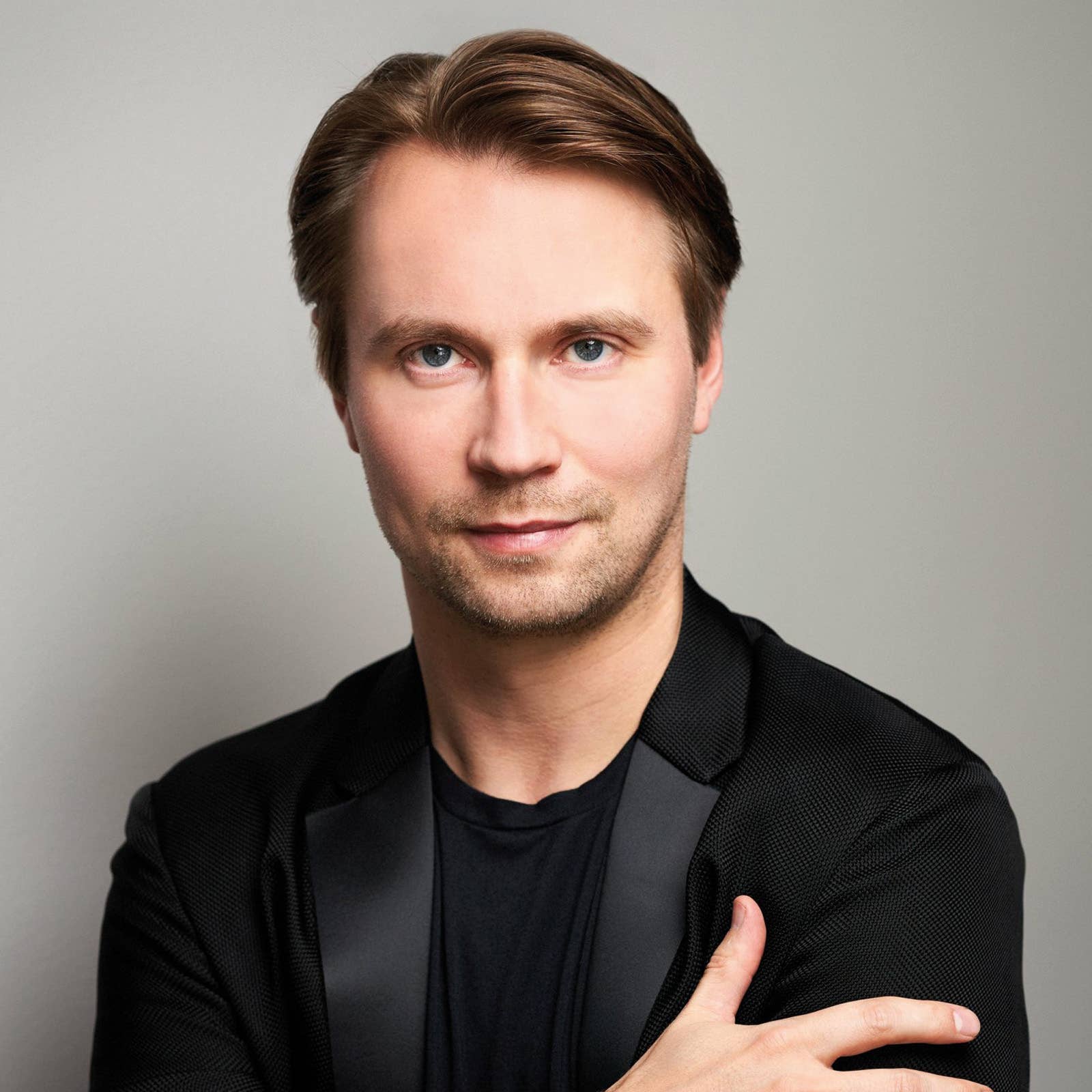 Smiling man with blue eyes and neatly styled brown hair wearing a dark blazer and shirt against a light background