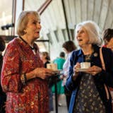 Two older women chatting over tea at an indoor café, holding cups and smiling.
