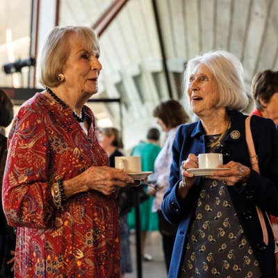 Two older women chatting over tea at an indoor café, holding cups and smiling.