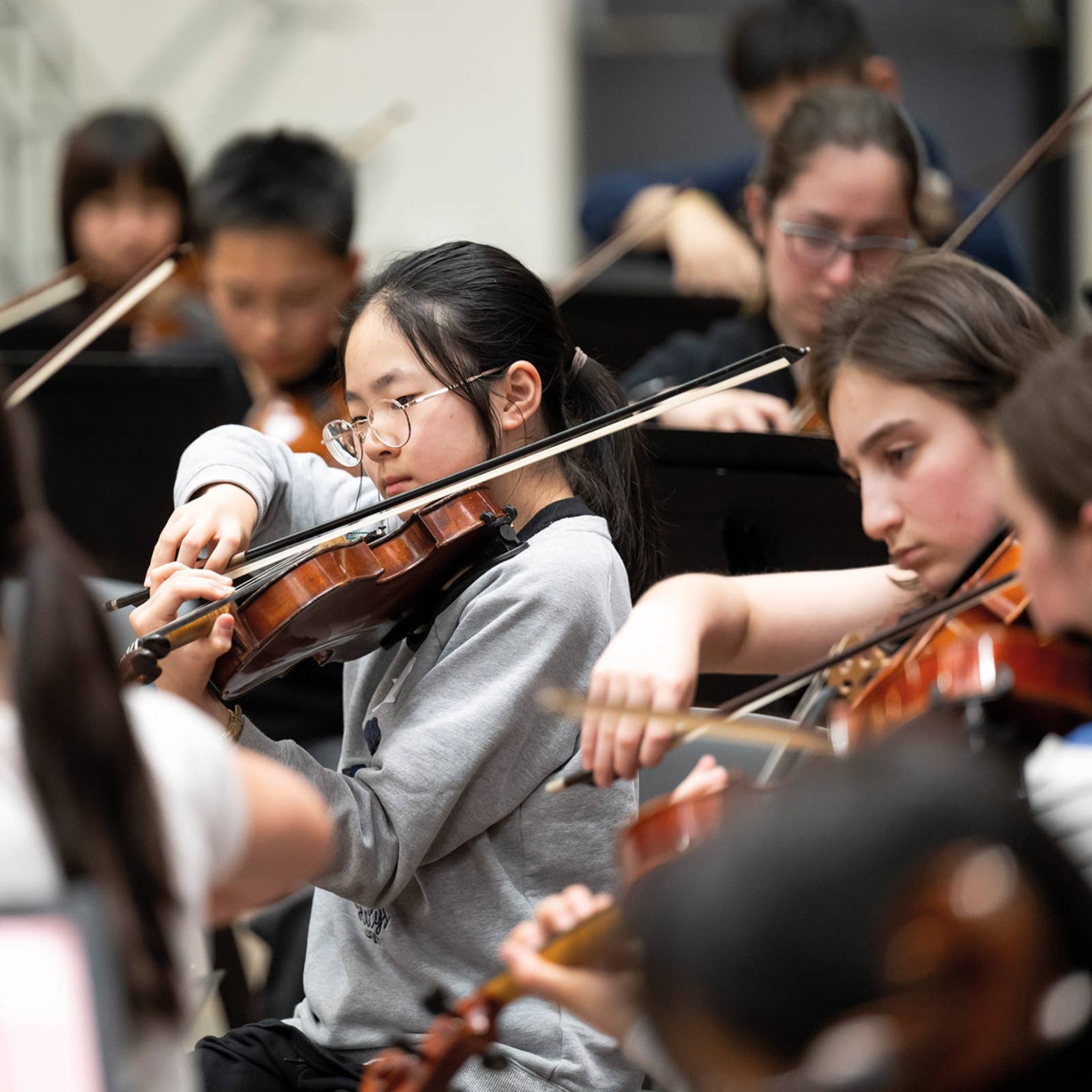Students playing violins in an orchestra, focused and engaged in their performance.