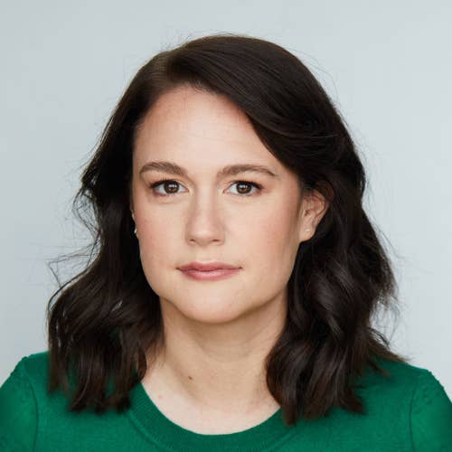 Close-up portrait of a woman with long dark hair, expressive eyes, and a slight smile against a light background.