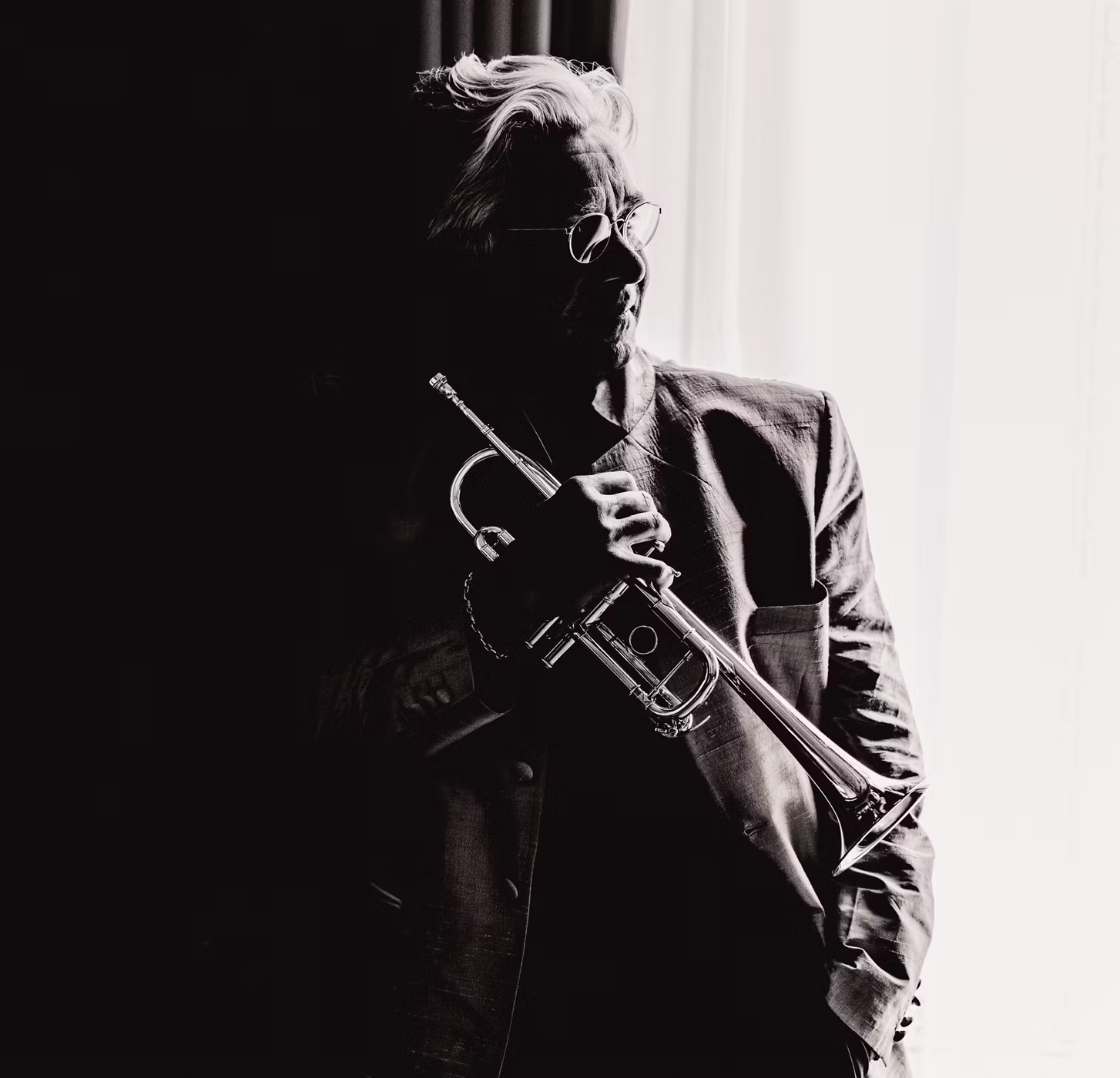 Black-and-white silhouette of a musician holding a trumpet, wearing glasses and a dark suit.