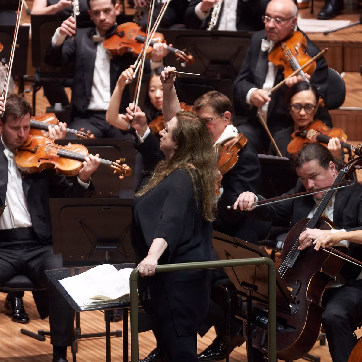 Orchestra musicians in black suits play violins and cellos on a concert hall stage during a live performance