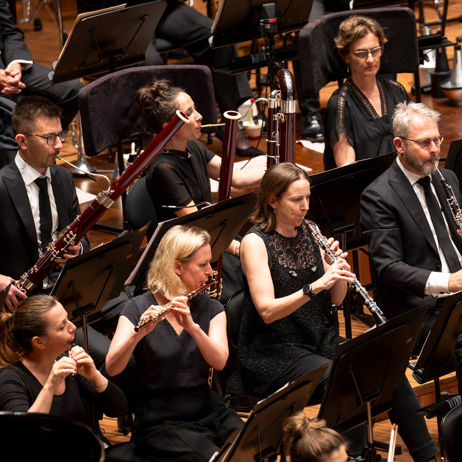 Musicians in an orchestra seated with clarinets and oboes, reading from music stands during a live performance.