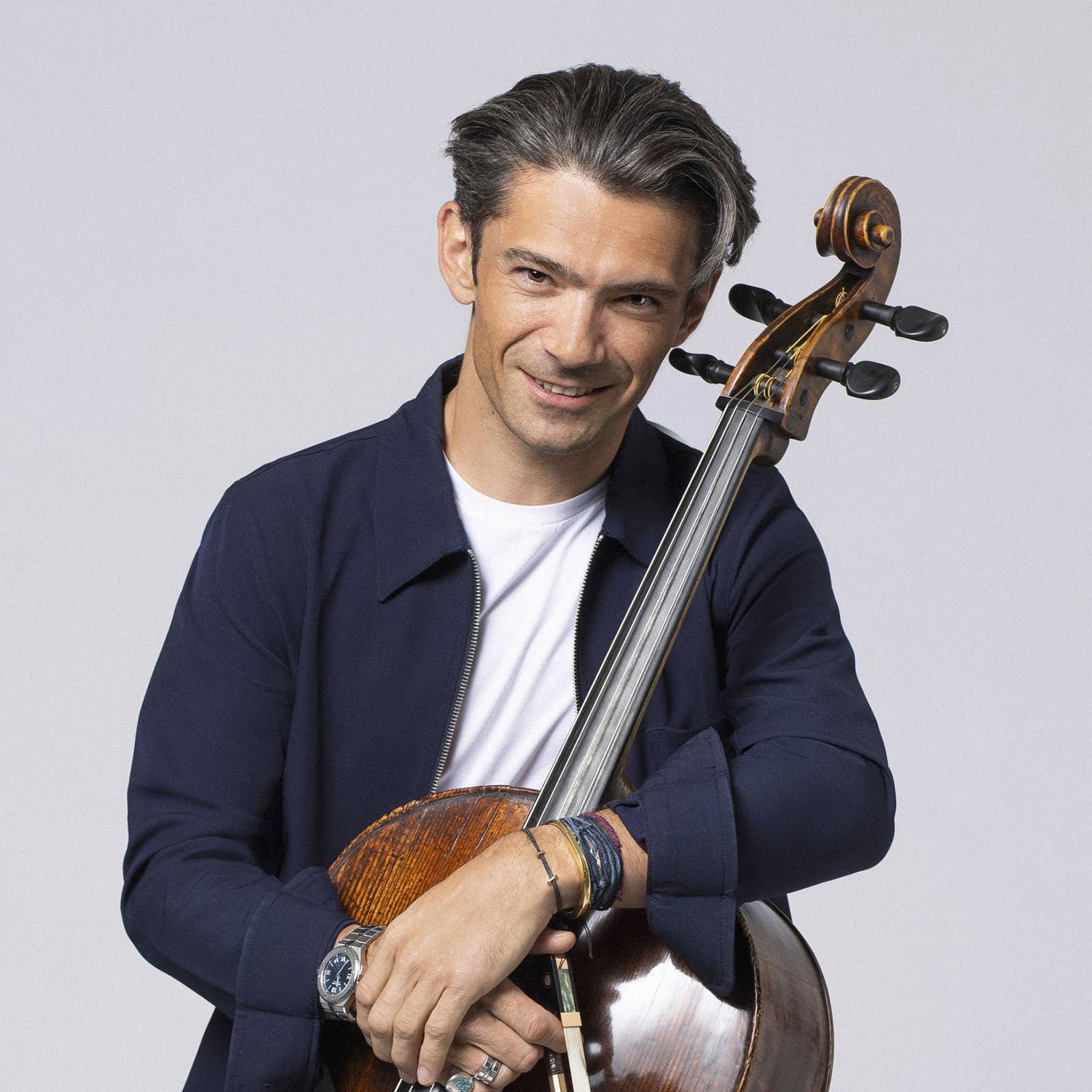 Smiling man holding an upright double bass against a light gray studio background