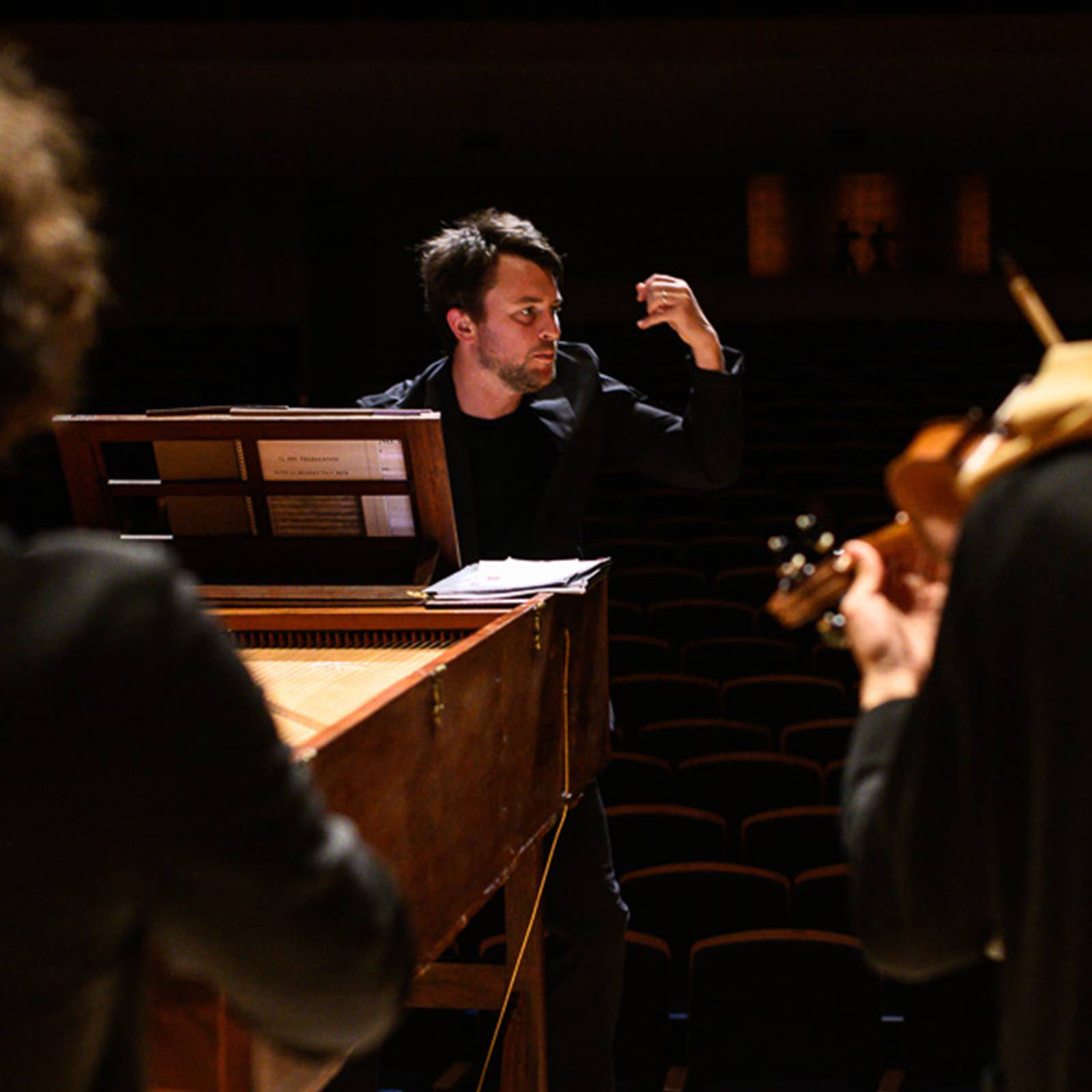 Musician in suit gesturing behind a piano during a live performance in a dim theater.