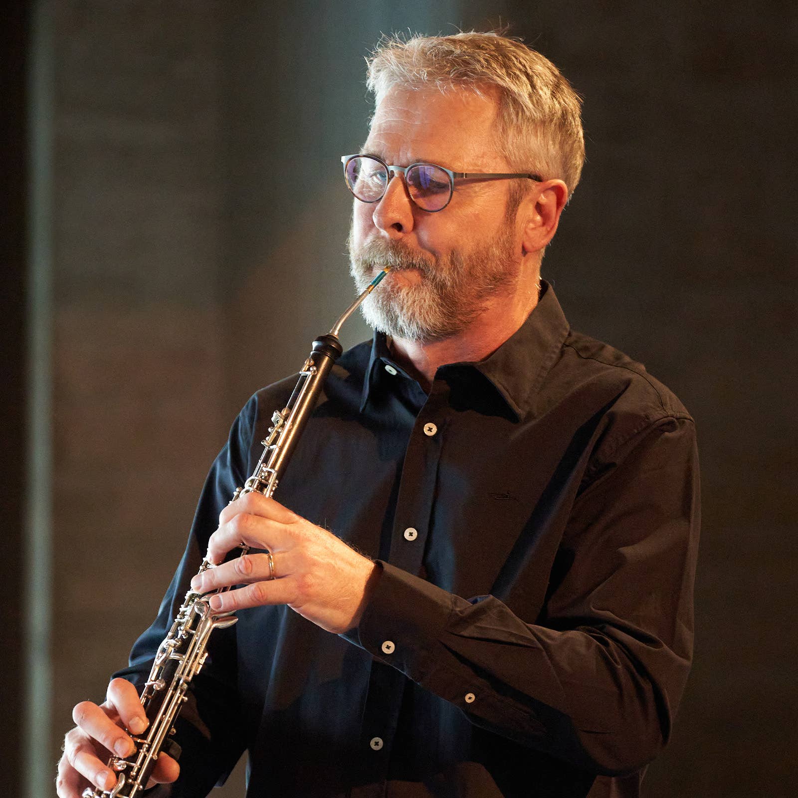 Man with glasses playing a brass wind instrument on stage under warm lighting