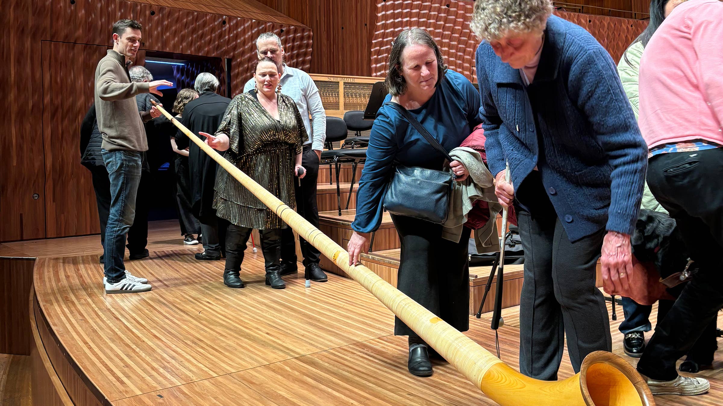 Audience members on theater stage, standing behind an alphorn during an event.