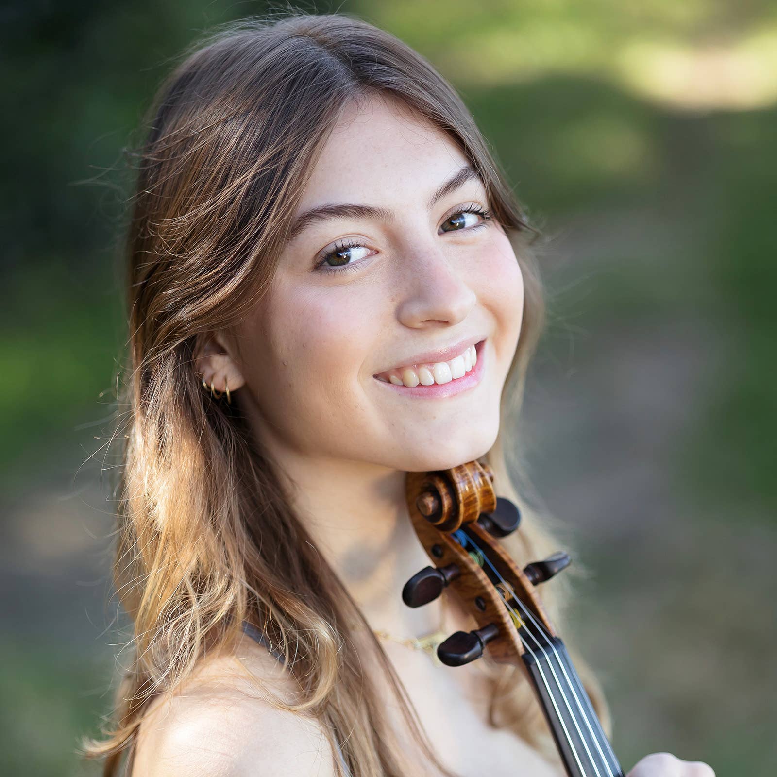 Smiling young woman holding a violin, outdoor portrait with blurred green background