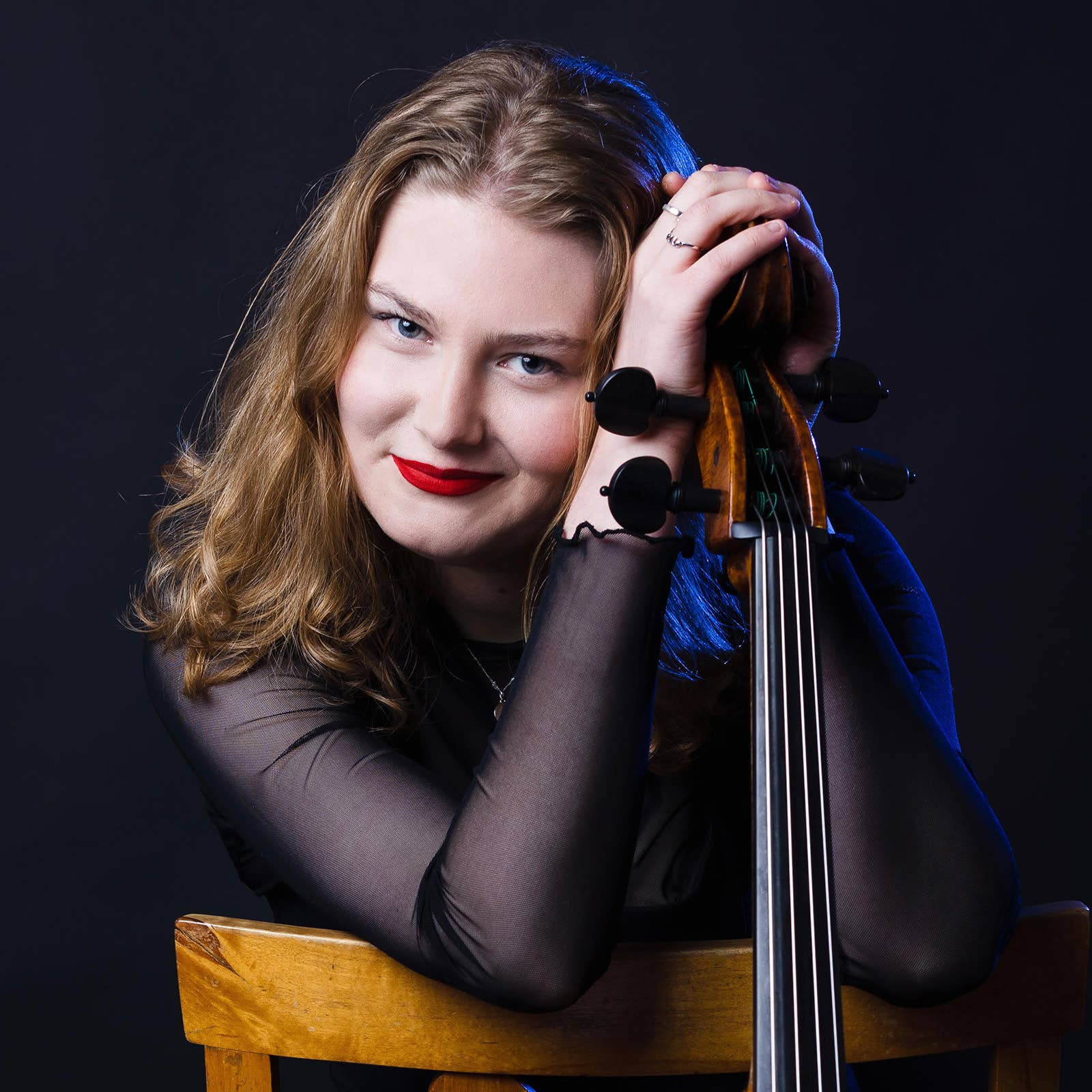 Woman with blonde hair wearing red lipstick, holding a hand at the side of a cello.